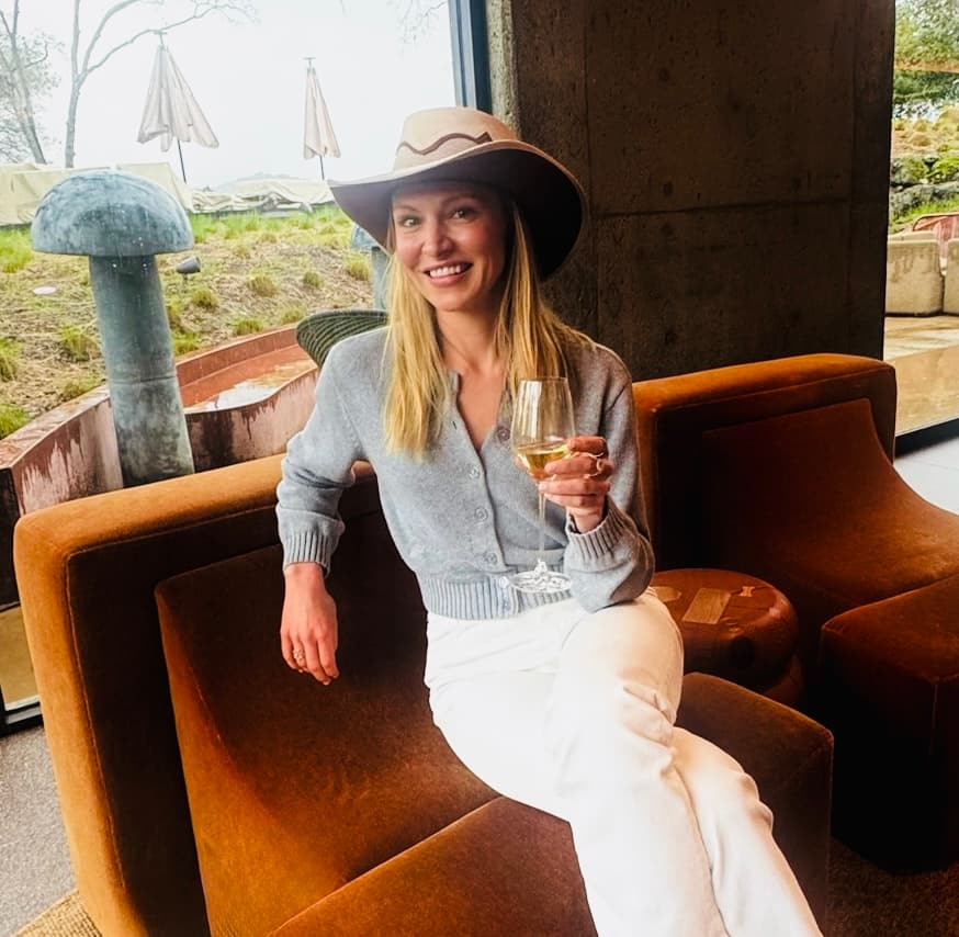 Maegan smiling, seated, wearing a cowboy hat and holding a glass of wine